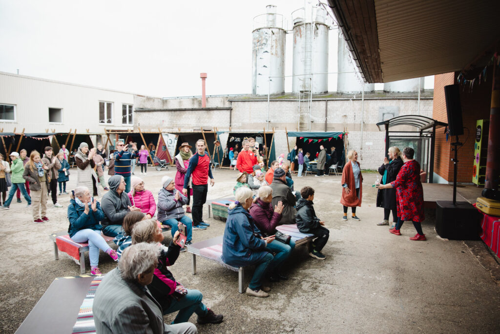 Inimesed festivali lava ees istumas, taustal telgid.